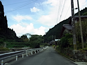 左にガードレールを隔てて剣持川の流れがある、右には民家が並んでいる